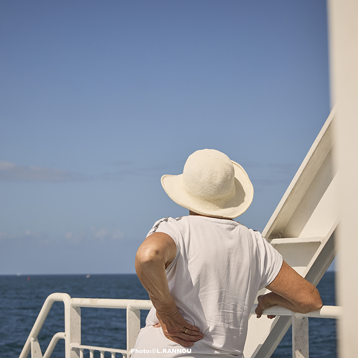 Photographe Bretagne – femme au chapeau contemplant l’océan depuis le pont du bateau à Lorient.